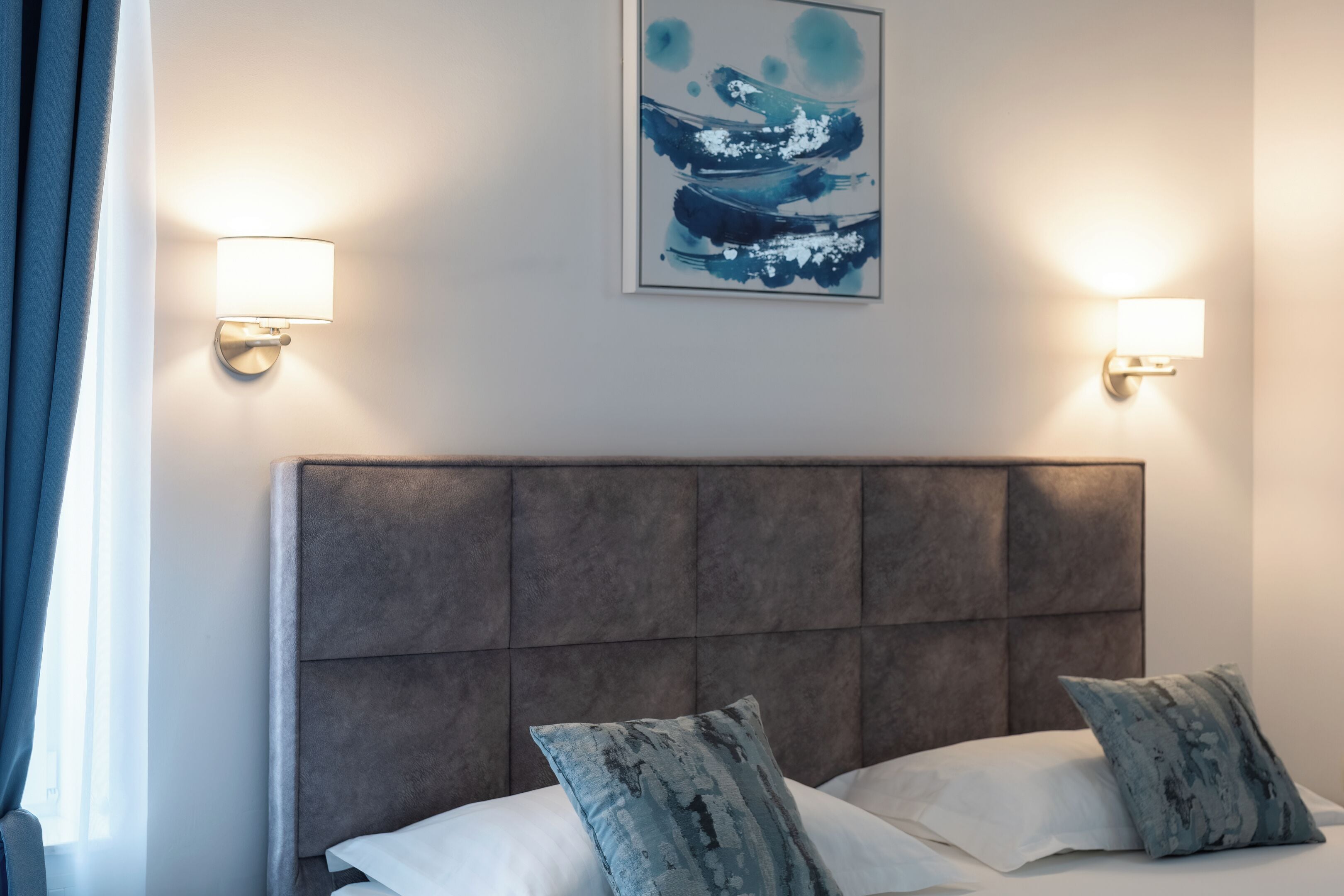 Une chambre d’hôtel avec un grand lit, deux lampes fixées au mur et une œuvre d’art abstraite accrochée au mur.