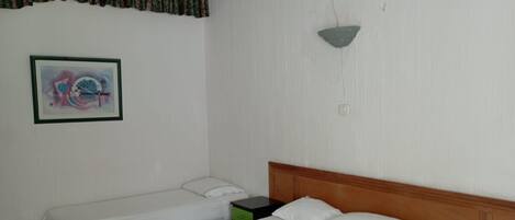 A room with two single beds, a green nightstand, a wall-mounted air conditioner, and a framed abstract painting.