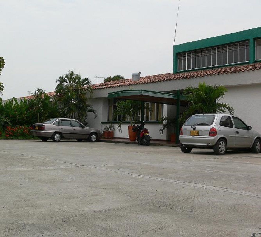 A building with a covered entrance, two parked cars, and potted plants.