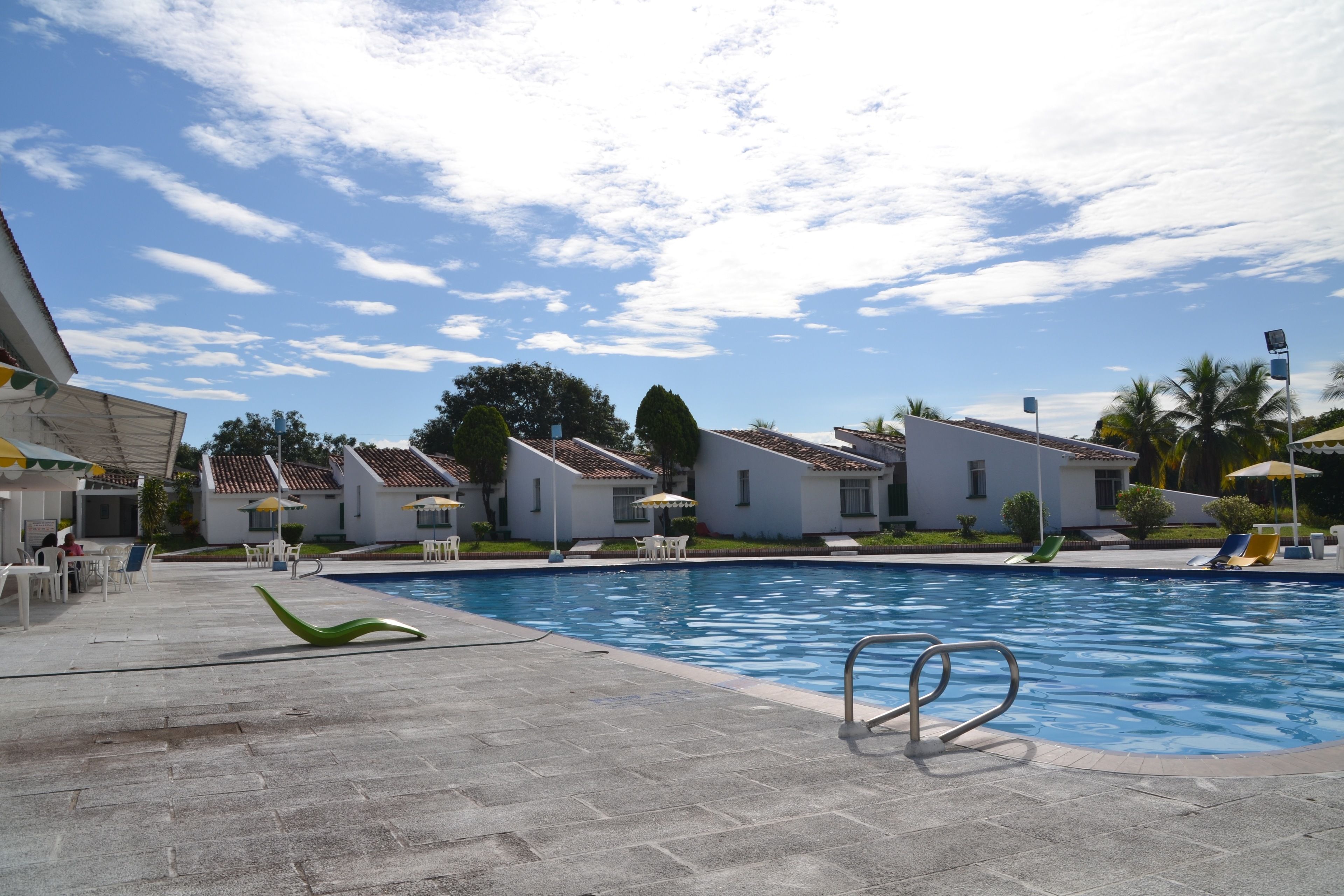 A swimming pool area with lounge chairs and umbrellas, surrounded by white buildings with tiled roofs.