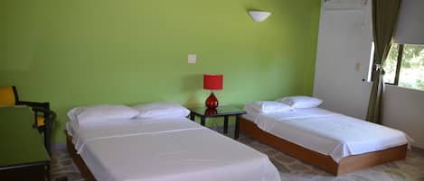 A room with two single beds, a small table with a red lamp, and a green wall.