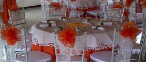 Una mesa redonda con sillas, cada silla tiene una cubierta blanca y tela naranja en la parte inferior.