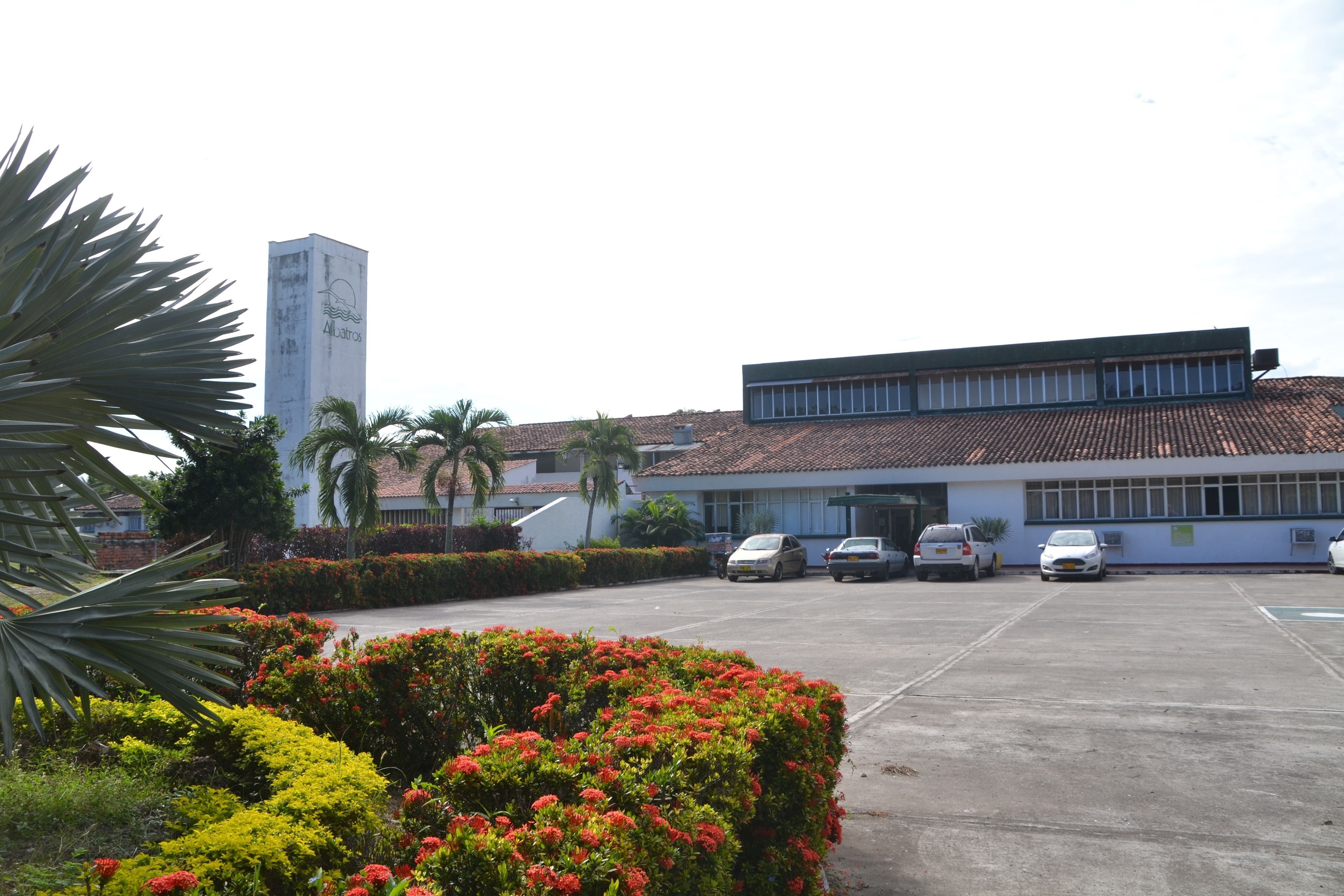 A building with a parking lot, several parked cars, and a garden with red flowers.