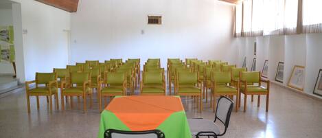 A conference room with rows of chairs, a table with a green and orange tablecloth, and framed pictures on the walls.