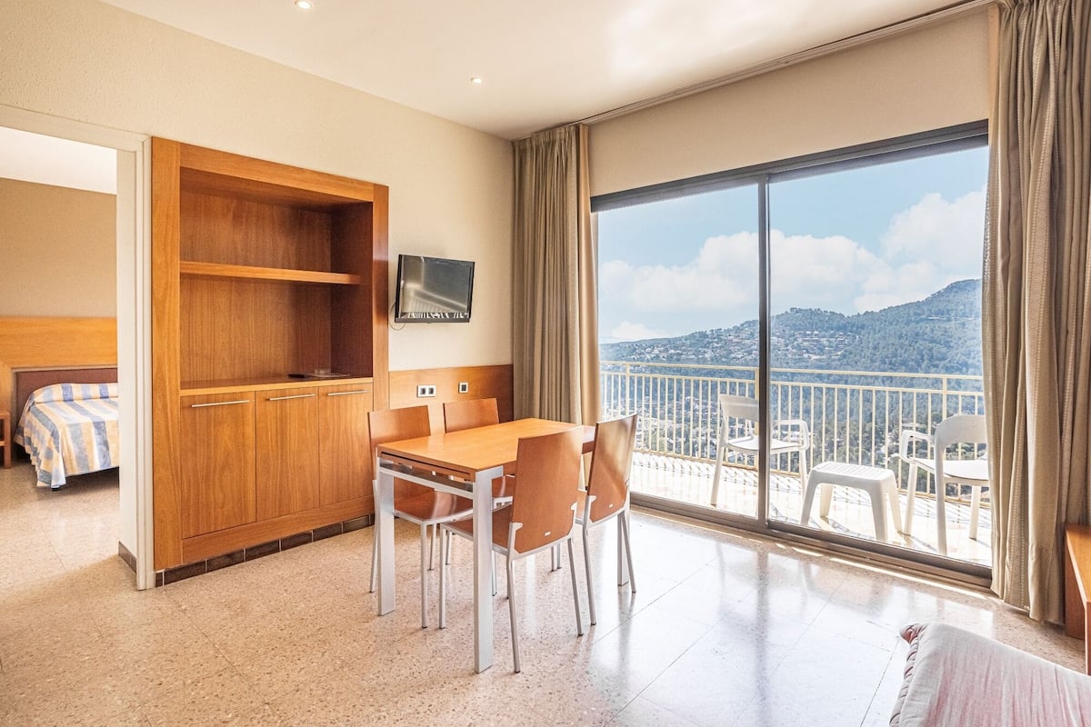 A hotel room with a balcony, a dining area, and a bed.