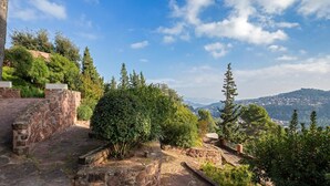 Un camino de piedra que asciende con vistas a un pueblo distante y un cielo azul despejado.