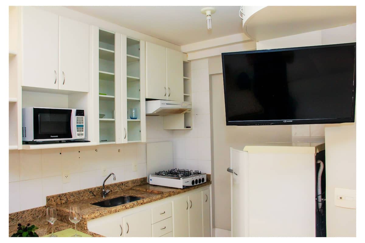 A kitchen with white cabinets, a microwave, a gas stove, a sink, and a flat-screen TV mounted above the stove.