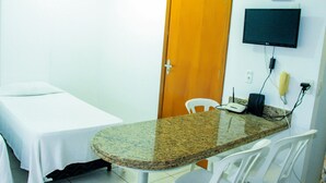 Une pièce comprenant un lit, une petite table, une chaise, un téléviseur fixé au mur et une porte.