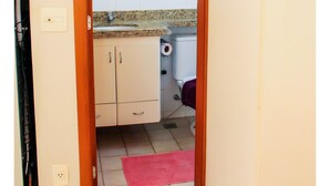 Un couloir étroit mène à une salle de bain équipée de toilettes, d’un lavabo et d’un miroir fixé au mur.