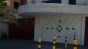 Une entrée d’immeuble avec une façade carrelée, des bollards et un panneau indiquant l’emplacement réservé au stationnement des visiteurs.