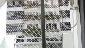 A room with a Samsung air conditioner mounted on the wall, a window with a metal grid, and a curtain. - Apartamento 3 quartos Bueno (Goiania)