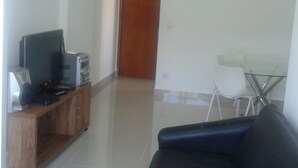 A living room with a black leather sofa, a wooden entertainment unit with a television, and a dining area with a glass table and chairs. - Apartamento 3 quartos Bueno (Goiania)