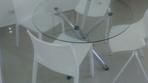A round glass table with four white chairs. There is a framed picture on the wall. - Apartamento 3 quartos Bueno (Goiania)