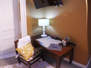 A small wooden desk with a white table lamp, a lace table runner, a framed photo, and a small candle holder.