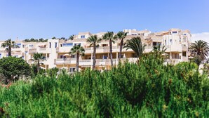 Un hotel de varios pisos con balcones, palmeras y un cielo azul despejado.