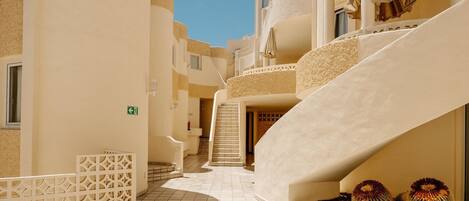 A hotel corridor with a curved staircase, tiled flooring, and a clear sky.