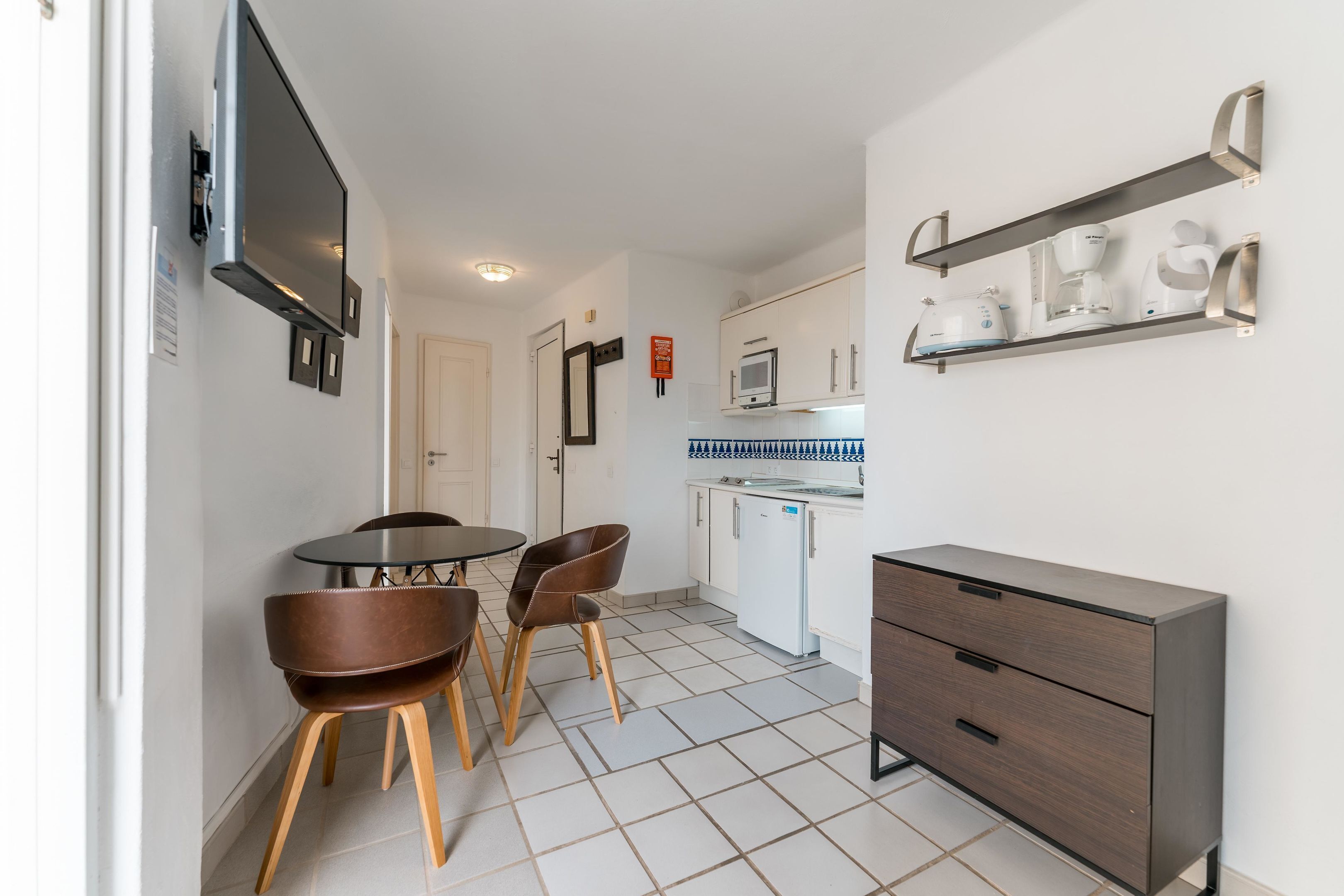 A compact kitchen with a dining area, a built-in oven, and a coffee machine on a shelf.