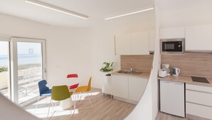 Una cocina moderna con armarios blancos, microondas y lavavajillas. Hay un balcón con vista al mar.