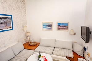 A cozy room with a striped sofa, a small table with a bottle and glasses, and two framed pictures on the wall. - R2 Maryvent Beach Apartaments (Pajara)