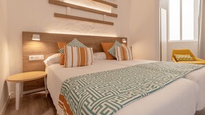 Una habitación de hotel moderna con una cama grande, una mesita de noche, una silla y un ventanal con cortinas.