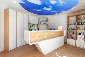 A reception desk with a clear view of the sky through the ceiling, a reception area with a bookshelf, and a sign indicating 'Apartamentos Maryvent RECEPTION'. - R2 Maryvent Beach Apartaments (Pajara)