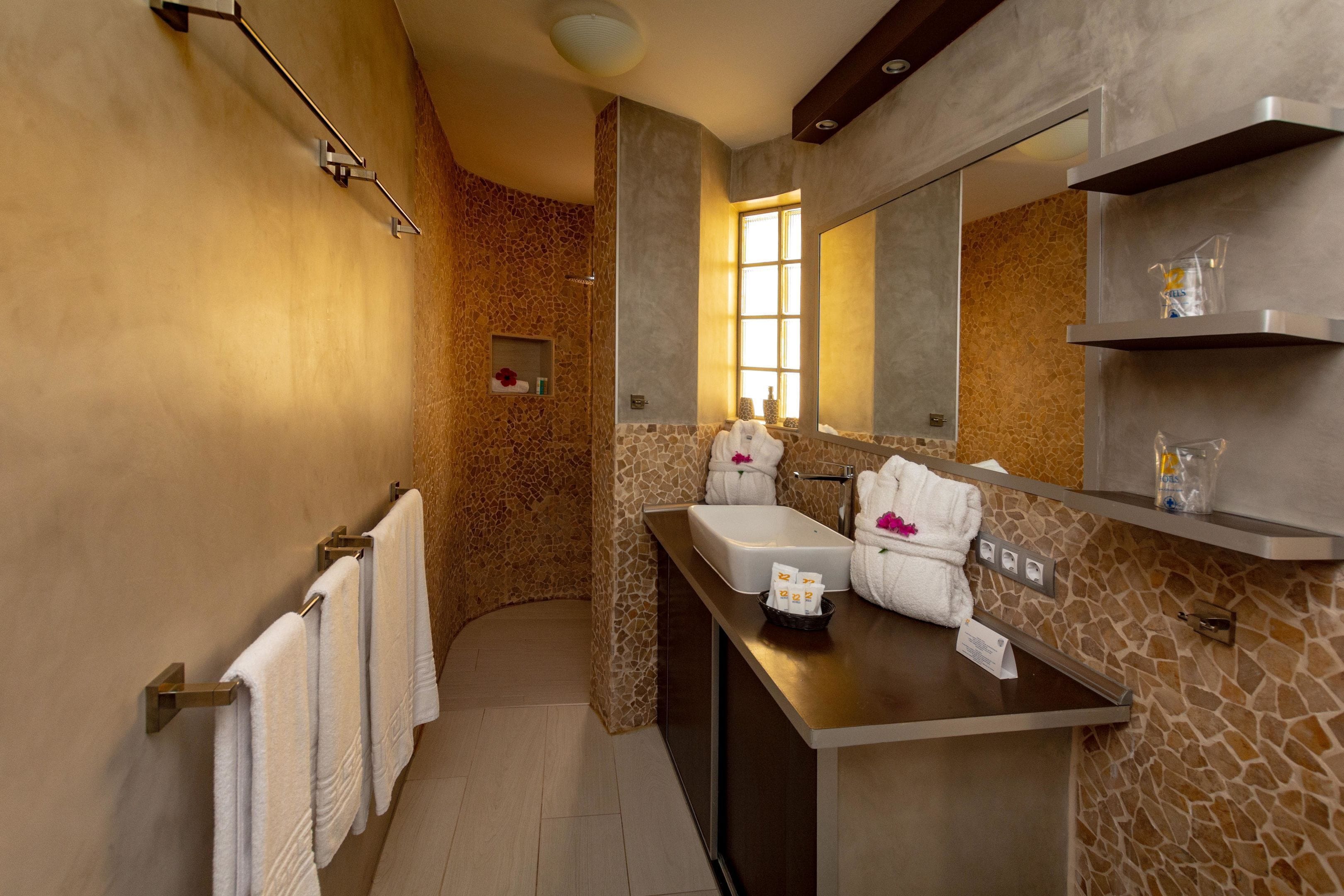 A modern bathroom with a stone wall, a large mirror, a sink, and a towel rack.