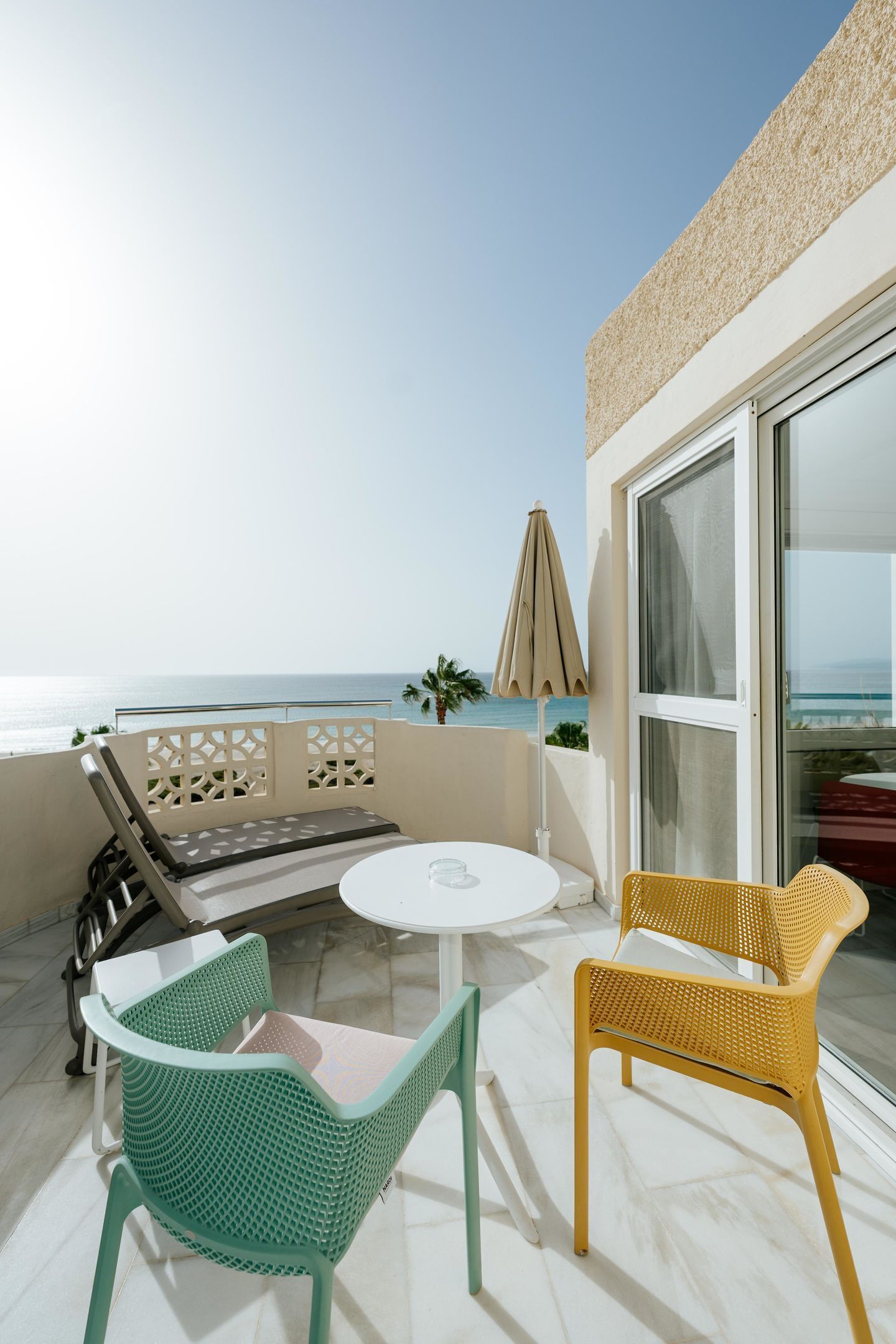 A balcony with a white table and chairs, a glass door, and a view of the sea.