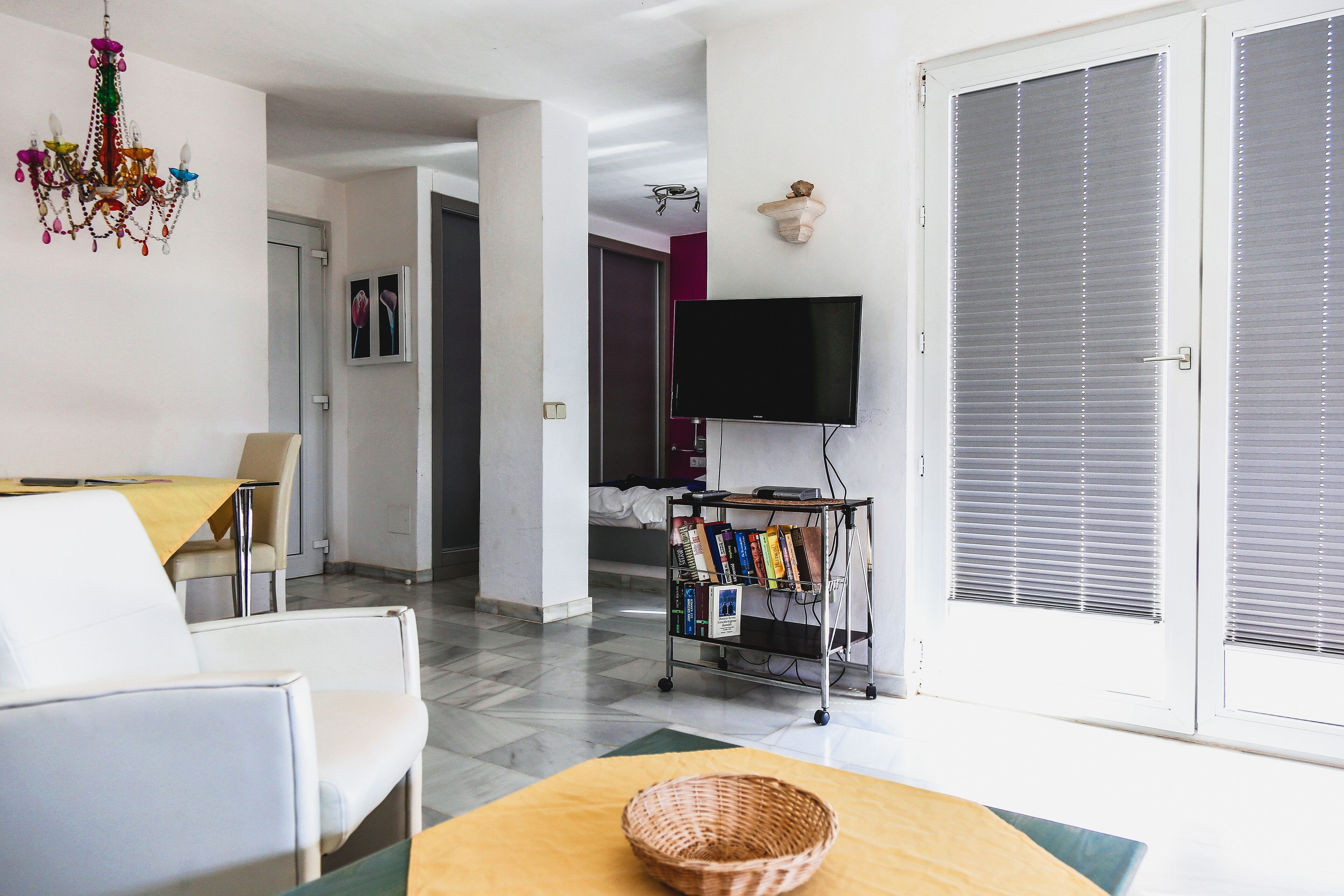 A living room with a TV, a bookshelf, and a dining area with chairs and a table.