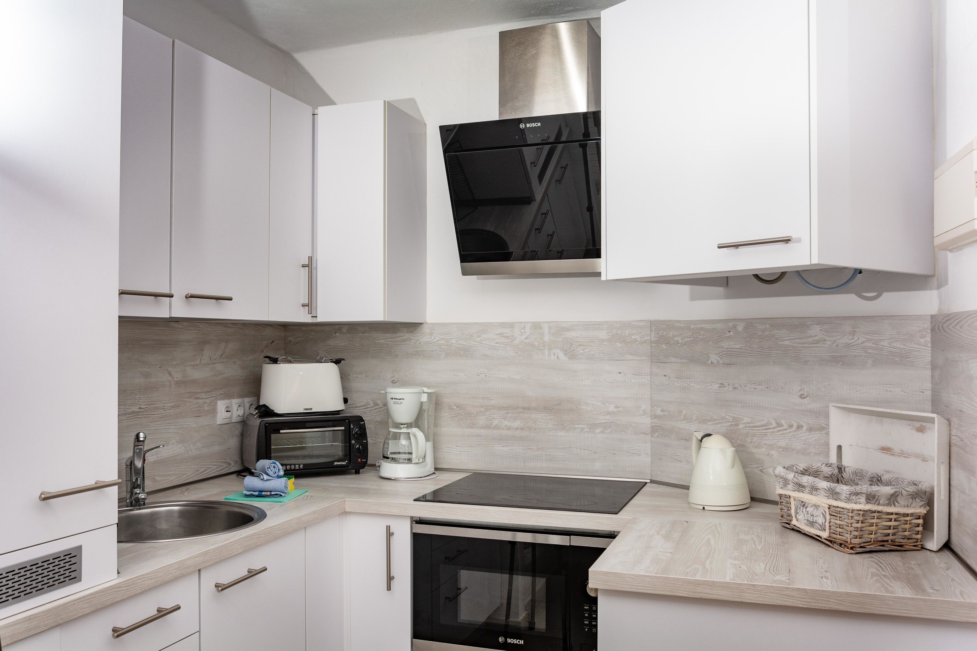 Una cocina moderna con armarios blancos, una campana extractora Bosch, un tostador, una cafetera y un lavavajillas.
