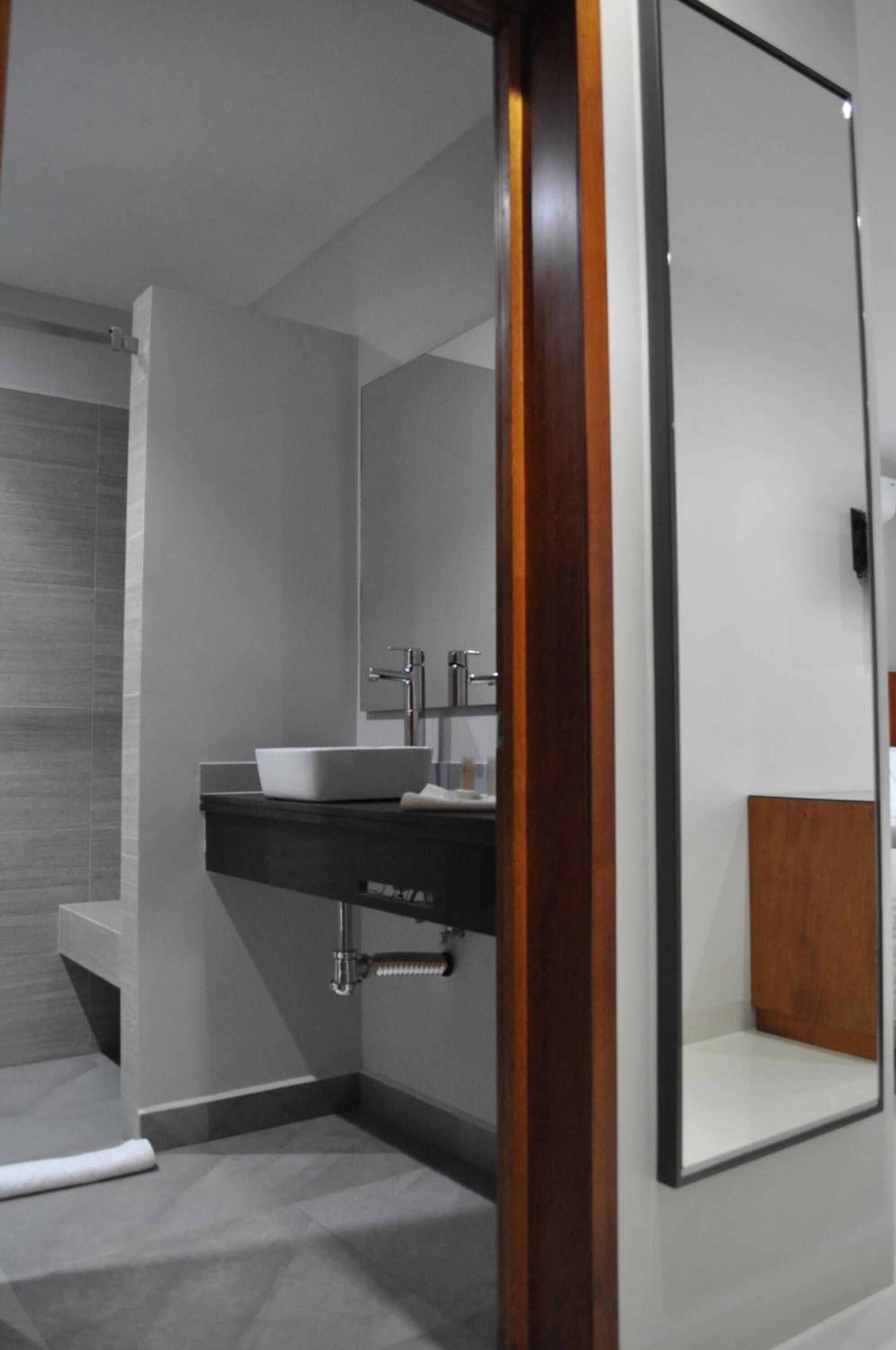 A modern bathroom with a white sink, mirror, and wooden accents.