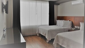 Una habitación de hotel con dos camas, un escritorio, un espejo y una ventana con cortinas.