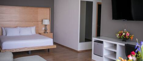 A modern hotel room with a bed, a desk, a flat-screen TV, and a small table with flowers.