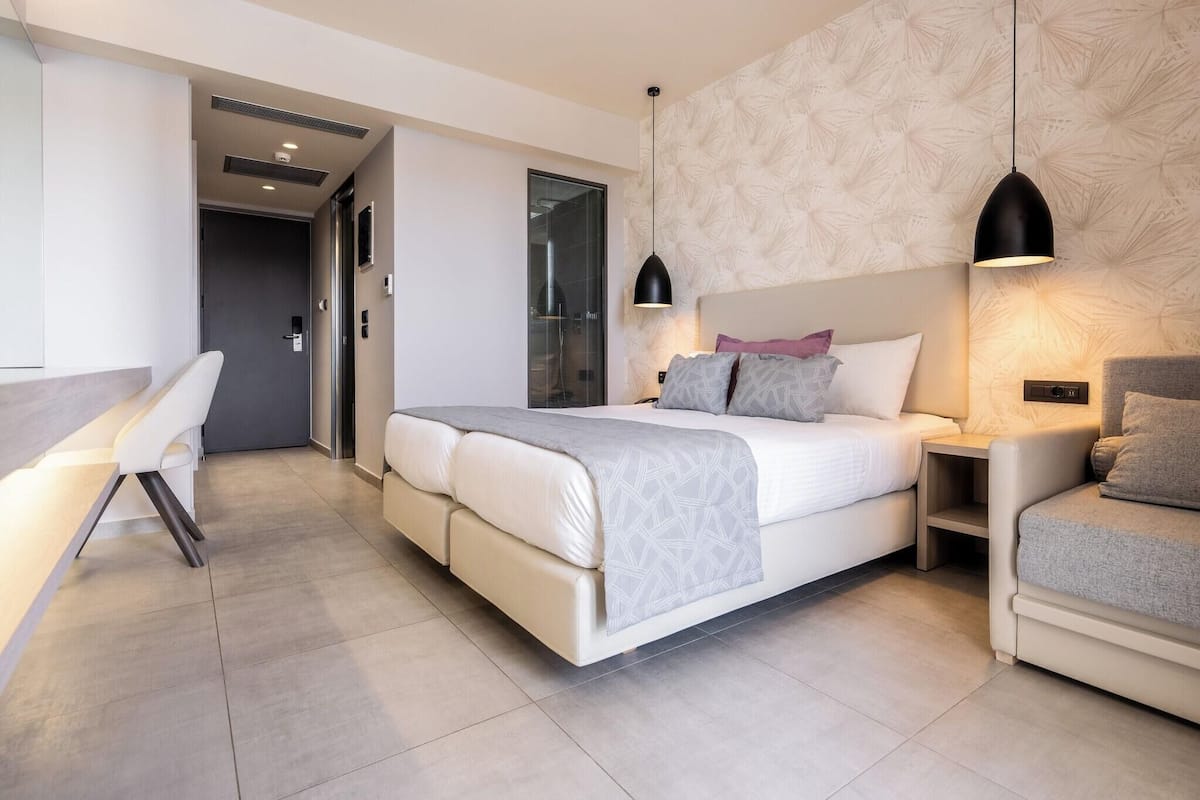 Quarto moderno com cama grande, mesas de cabeceira, escrivaninha e parede estampada.