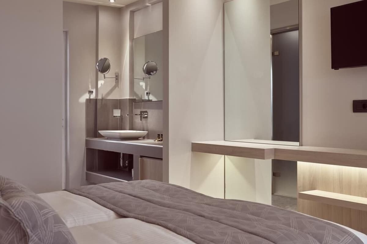 A modern bedroom with a large bed, a bedside table, a built-in vanity with a mirror, and a wall-mounted TV.