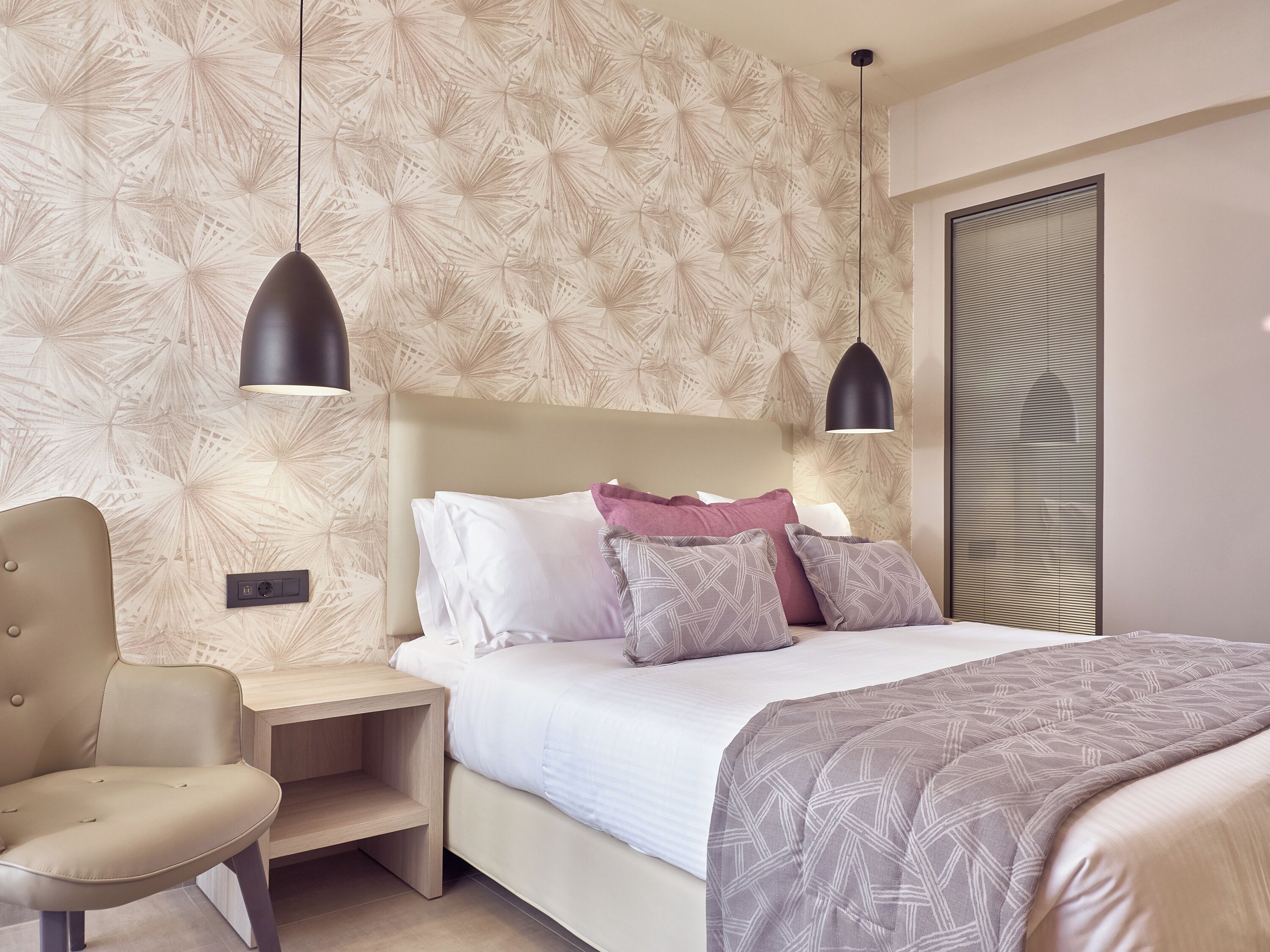 Una camera da letto moderna con un letto, comodini, una sedia e carta da parati decorata.
