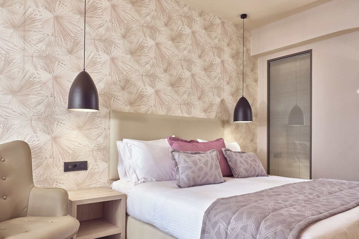 Quarto moderno com cama, mesas de cabeceira, uma cadeira e papel de parede estampado.