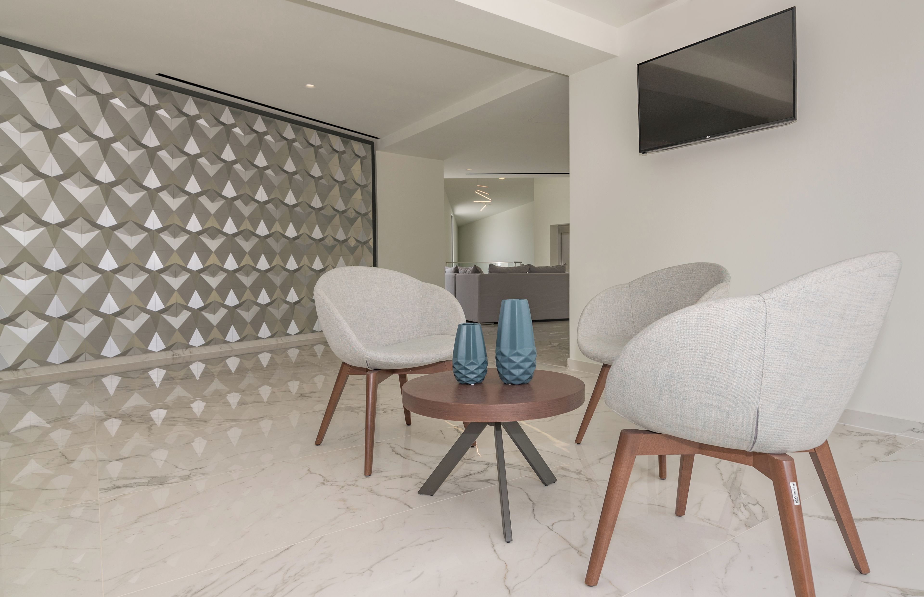 A modern living room with a marble floor, two grey armchairs, a small round table with blue vases, and a geometric-patterned partition.
