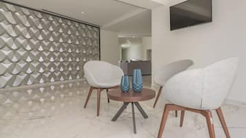 A modern living room with a marble floor, two grey armchairs, a small round table with blue vases, and a geometric-patterned partition.
