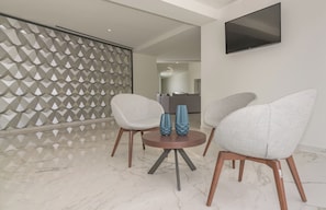 Een moderne woonkamer met een marmeren vloer, twee grijze fauteuils, een klein rond tafeltje met blauwe vazen en een scheidingswand met een geometrisch patroon.
