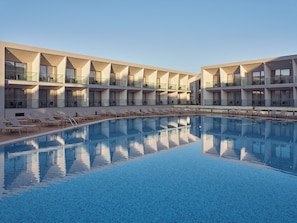 Een modern hotel met een centraal gelegen zwembad, meerdere balkons en ligbedden.