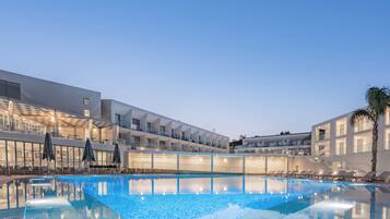 Un hotel moderno con piscina, mobiliario exterior y fachada luminosa.