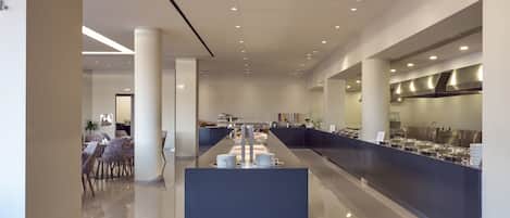 Un moderno vestíbulo de hotel con un mostrador de recepción central, zona de estar y una cocina a la vista al fondo.