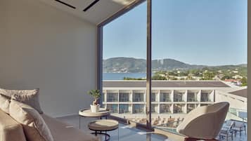 A modern hotel room with a large balcony, a sofa, a small table, and a chair.