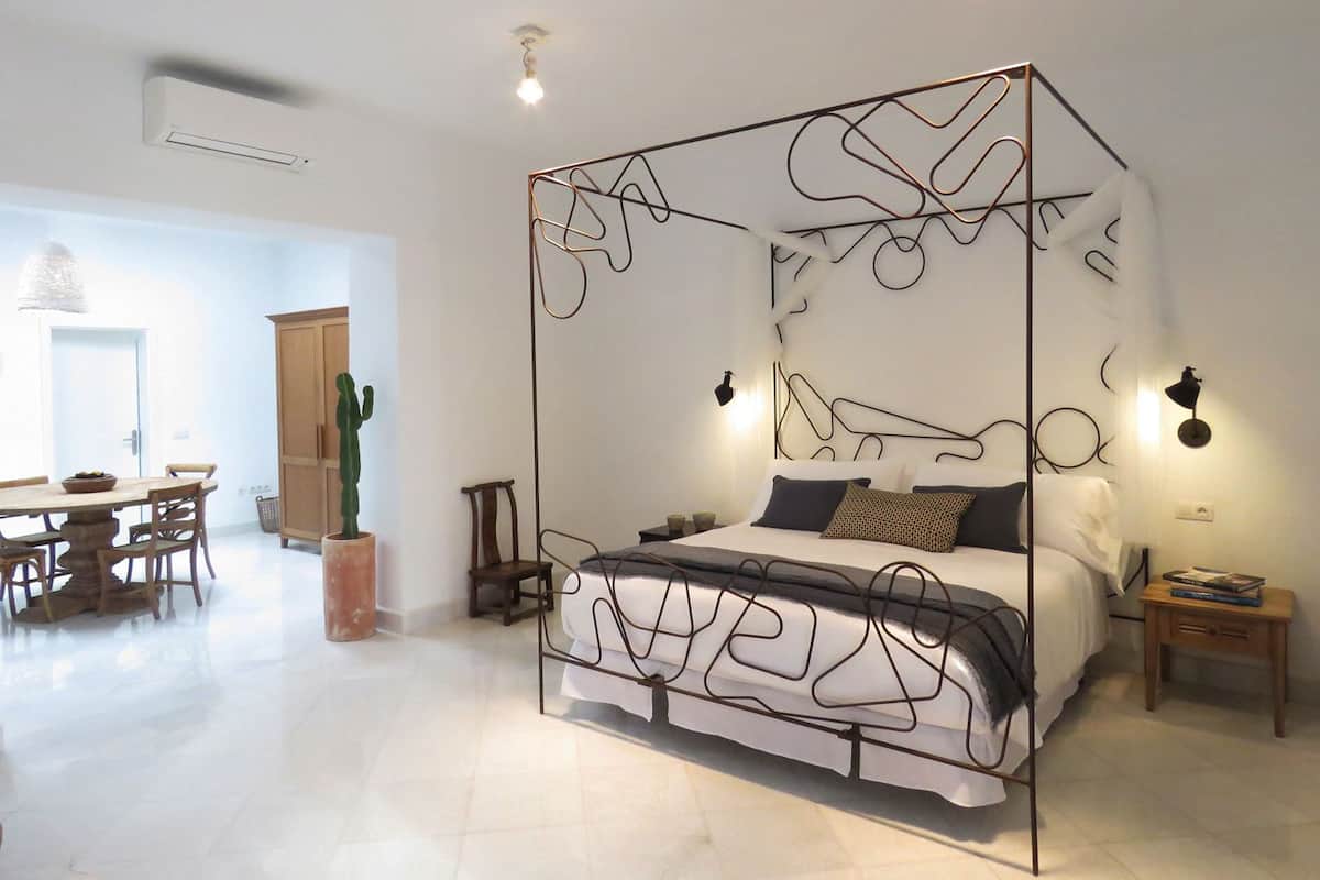 A bedroom with a four-poster bed, a dining area with a table and chairs, and a cactus plant.