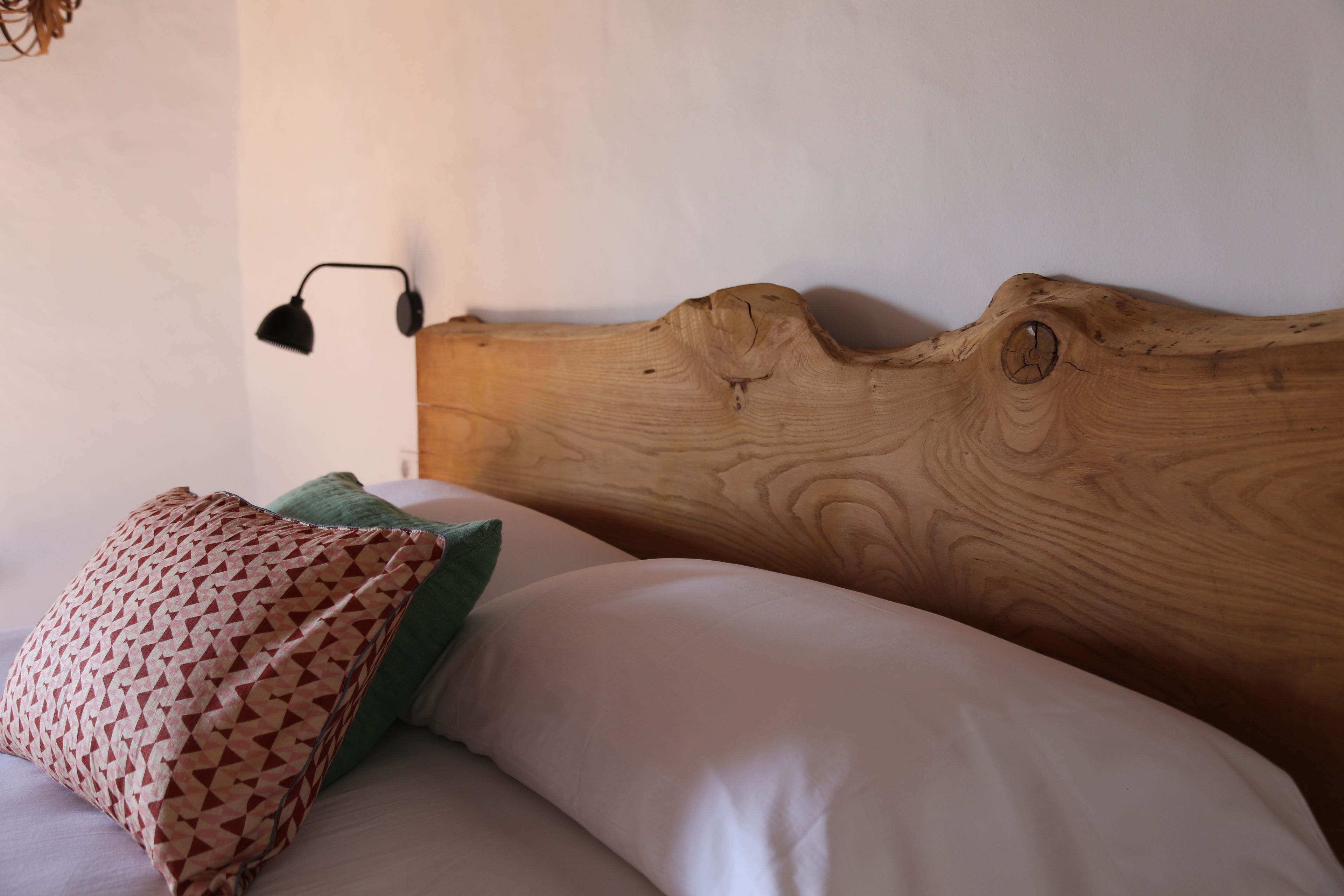 Una cama con cabecera de madera, un cojín estampado y un cojín verde.