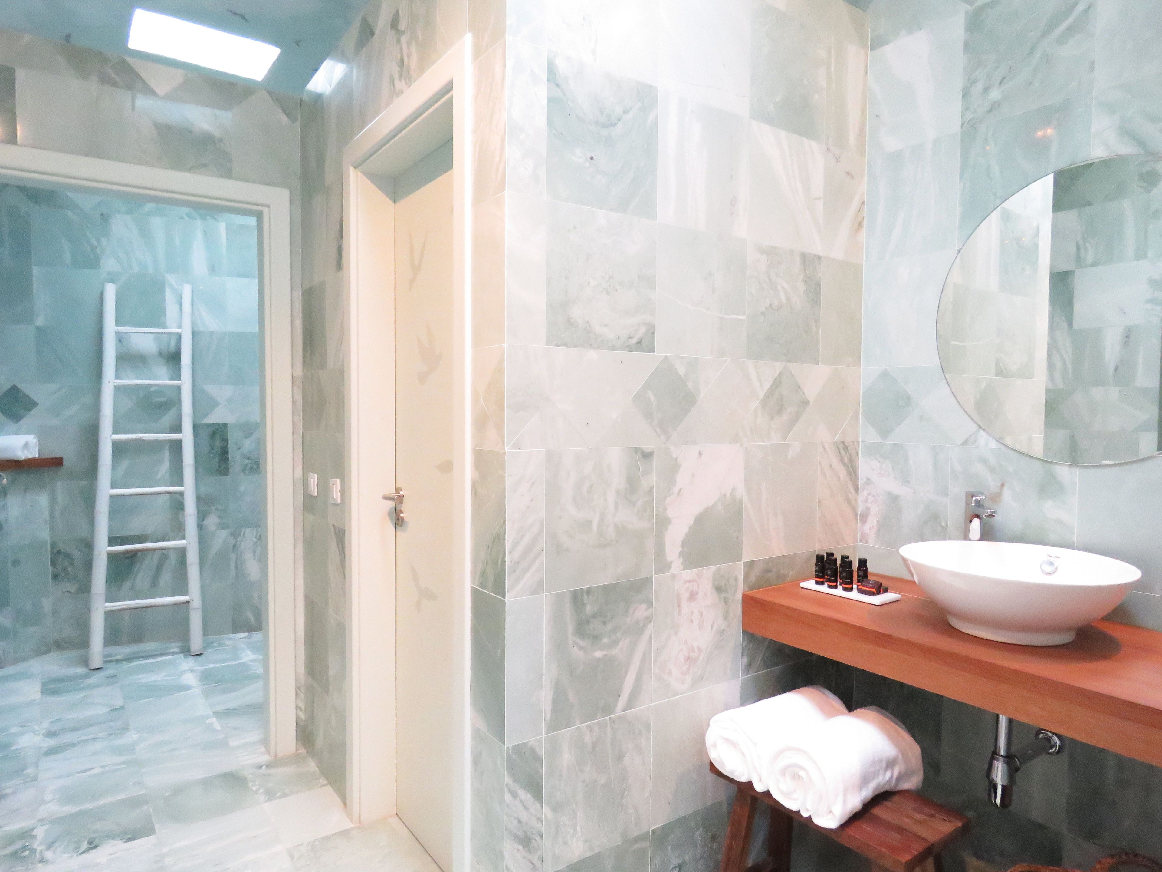 A bathroom with a marble floor, a wooden stool with a towel, a white sink, and a mirror on the wall.