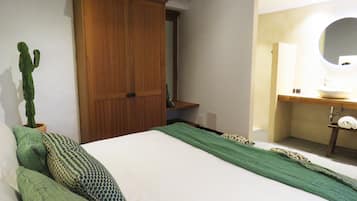 Un dormitorio con cama, armario de madera, planta verde y baño con lavamanos y espejo.