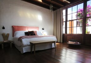A bedroom with a large bed, wooden floor, and a window with a view of flowers.