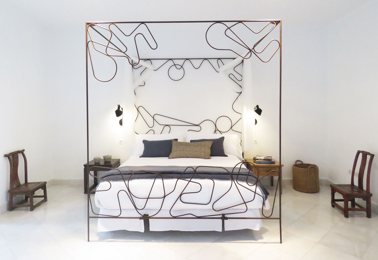 A modern bedroom with a unique metal frame bed, two bedside tables, and a nightstand.