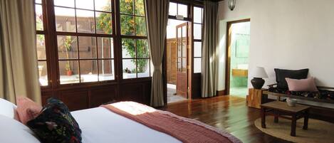 Un dormitorio con una cama grande, un banco de madera, una mesita y vistas al exterior a través de amplias ventanas.